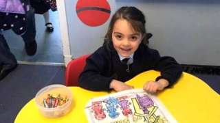 Mia Kasravi at a table in her school, drawing a picture with crayons