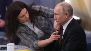 An assistant helps fix Russian President Vladimir Putin's mic