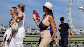 People walk along Westminster bridge on 3 September, image shows a group of mixed gender people, one of them fanning themselves to cool down from the heat.