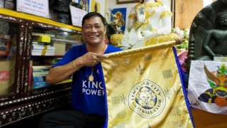 Korpsin Uiamsa-ard, an assistant of chief monk Phra Prommangkalachan at the Wat Traimitr Withayaram temple, holds up a Leicester City banner in Bangkok, Thailand, Tuesday, May 3, 2016