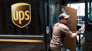 A UPS worker carries a box into a UPS truck in Miami - June 2023