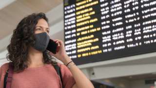 Stock image of a woman using a phone in front of an airport departure board