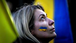 A demonstrator with the Ukrainian flag painted on the cheek looks on between flags during a protest against Russia's military operation of Ukraine, in front of Belem Palace in Lisbon, Portugal, on 26 February 2022