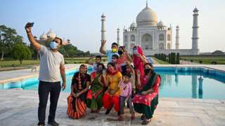 A group of tourists take photos as they pose in front of the Taj Mahal in Agra, India