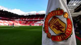 A corner flag showing the badge of Manchester United inside Old Trafford