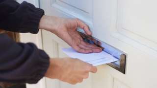 Close up of postman delivering post through a letterbox