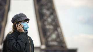 A woman wearing a surgical face mask walks near the Eiffel Tower