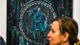 A woman walks past a Bitcoin themed art installation during the Bitcoin 2022 Conference at the Miami Beach Convention Center in Miami Beach, Florida, on April 7, 2022.