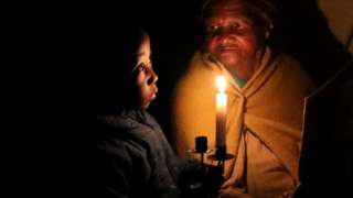 A woman and her great-grandson sit in candlelight.