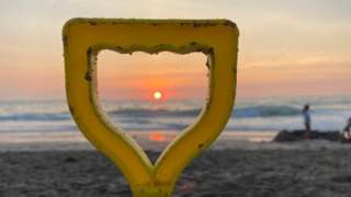 The sun setting over sea seen through a spade handle on a beach