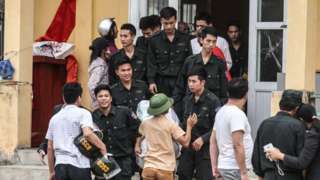 Các cảnh sát được thả (mặc đồng phục sẫm màu) bước ra khỏi đình làng tại xã Đồng Tâm, huyện Mỹ Đức, Hà Nội vào ngày 22 tháng 4 năm 2017.