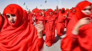 Sahrawi women perform a dance in the parade. They are fully clothed in red.