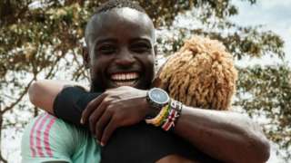 Ferdinand Omanyala embraces his wife and fellow sprinter Laventa Omanyala. He is smiling from ear to ear in a green top.