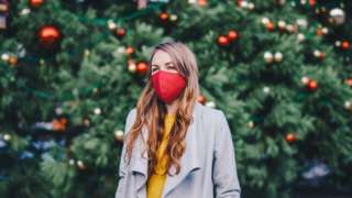 Women in face mask in front of Christmas tree