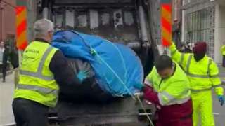 Refuse workers throw the tents into the back of the bin lorry