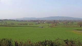 Image showing the land near Highleadon where JBM Solar Projects 21 Ltd wants to create a solar farm. There are very few houses on the large field and a blue tractor in the middle of it. More fields can be seen in the distance.