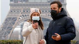 A couple wearing protective face masks takes a selfie in front of the Eiffel Tower during the coronavirus epidemic (COVID-19) on November 25, 2021 in Paris, France
