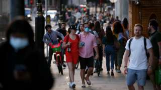 A man wearing a face mask walks along a busy Bridge Street outside Westminster Station as dusk falls at the end of a warm spring day in London