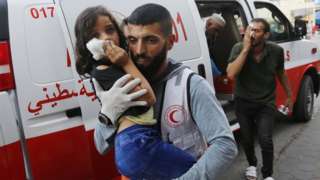 A man carries an injured child to Al Aqsa Martyrs Hospital