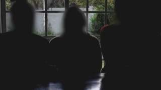 Silhouettes of three women in a dark room, with their faces blurred for anonymity