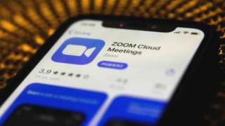 The Zoom app install screen is seen on a smartphone display, with the phone itself laid against