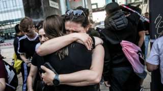 Two people hug each other in front of the Fields shopping mall where the shooting happened