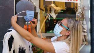 A woman places a mask on a mannequin outside a clothing store in Aranda de Duero, near Burgos on 7 August
