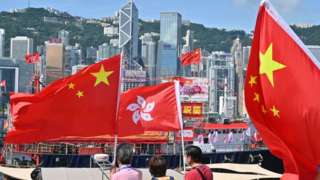 People wave Chinese and Hong Kong flags as fishing boats with banners and flags to mark the 25th anniversary of the Handover of Hong Kong from Britain to China sail through Hong Kongs Victoria harbour on June 28, 2022.