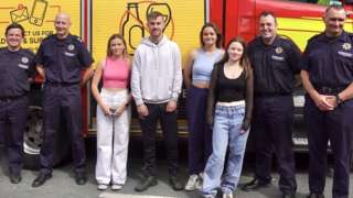 University students and firefighters stand in front of a fire engine