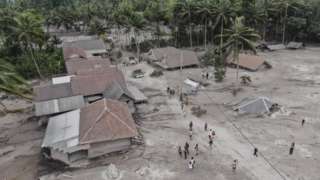 A handout image shows villagers looking at a village buried by ash