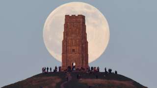 People stand beside St Michael"s Tower as they watch the full moon, sometimes known as a "Wolf Moon", rise behind Glastonbury Tor in Glastonbury, Britain, January 17, 2022