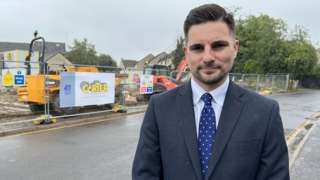 Councillor Joe Harris in a suit standing in front of a building site