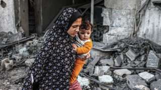 A woman holding a child flees following an Israeli strike in Rafah in the southern Gaza Strip on 23 November, 2023,