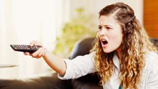 A stock image of a woman angry at the tv