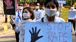 A woman wearing a face mask holds a sign that reads 'Stop rape' at a protest in Delhi