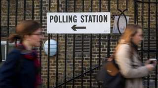 Women passing a "polling station" sign