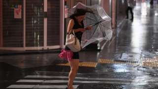 A woman struggles with an umbrella in the wind and rain