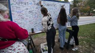 Attendees add their signatures to a board in support of survivors of sexual abuse at a vigil outside the home of outgoing University of Michigan President Mark Schlissel October 13, 2021 in Ann Arbor, Michigan