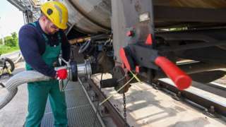A worker prepares to receive liquid additive for petroleum refining from a tanker train