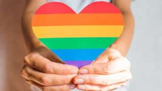 Hands holding a heart decorated in rainbow stripes