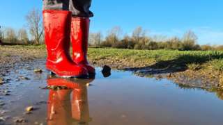 A child in red boots standing in a puddle