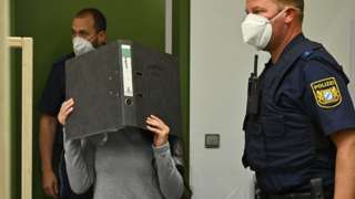 Jennifer Wenisch in court, covering her face with a folder, 13 Oct 21