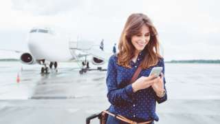 Woman using smartphone in front of aeroplane