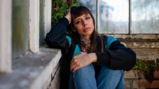 Kayla Painter sitting on the floor with an arm over her knees, leaning her head in her other hand against a wall