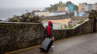 A person drags a suitcase along a street above Tenby harbour