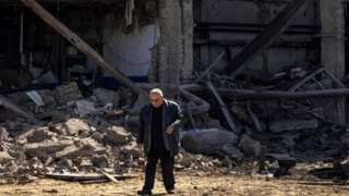 Image shows man walking among rubble