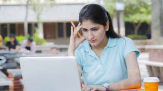 A model stares at a laptop, looking concerned