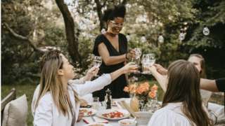 Five women toasting drinks at an outside dinner