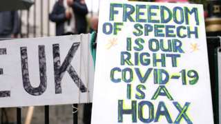 a placard reading 'freedom of speech is our right, covid-19 is a hoax'