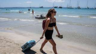 Woman with a suitcase walking along a beach